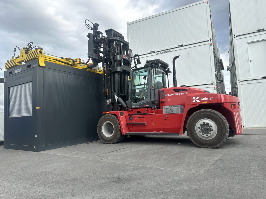 Der Kalmar DCG 120 mit Kaup-Spreader beim Handling eines Modulcontainers am Standort der Riedo Mobilbau AG in Gurmels FR. (Foto: pd)